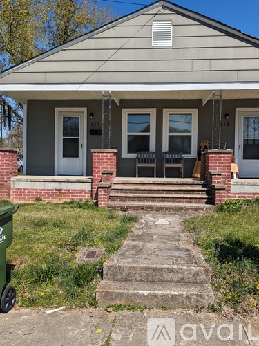 A house with a front porch and a green trash can in front of it.