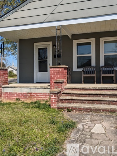 A house with a white door and two windows with a brick pillar in front.