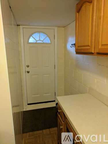 A white door with a window in the middle is in a hallway with wooden cabinets.