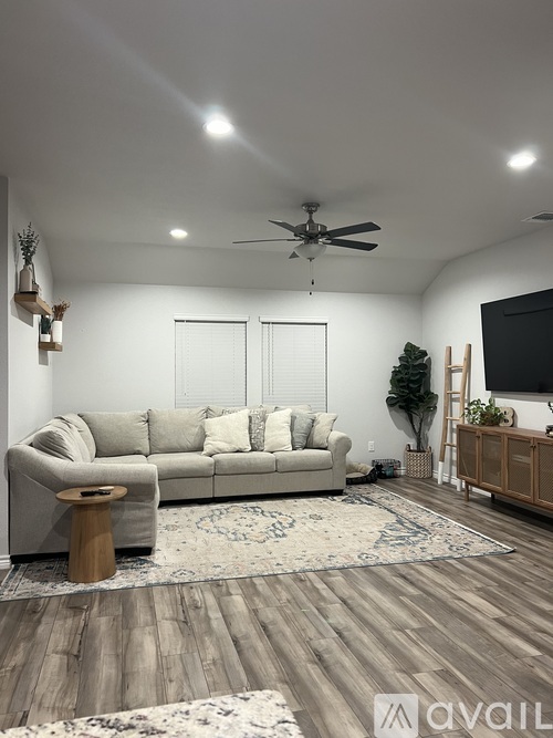 A living room with a couch, a rug, a ceiling fan, and a TV.
