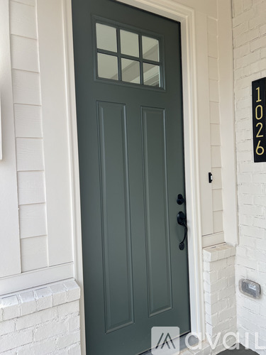 A dark green door with a glass panel is set in a white brick wall.