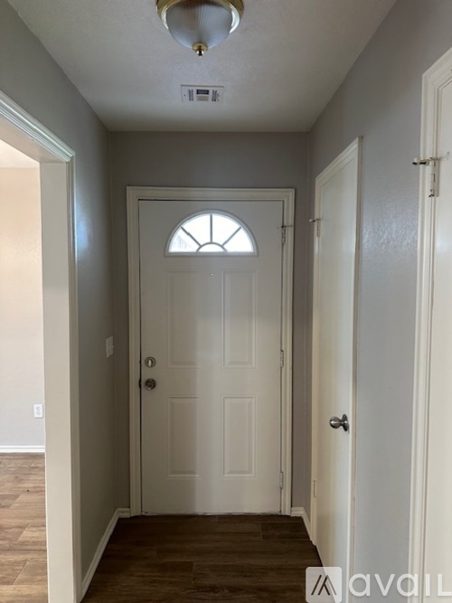 A white door with a window in the middle is in a hallway with wood floors.