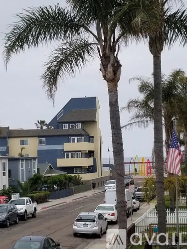 A street with cars and palm trees in front of a building.