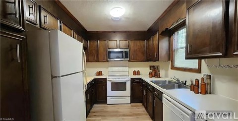 A kitchen with dark wood cabinets and white appliances.