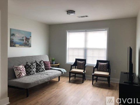 A living room with a grey couch, two chairs, and a painting on the wall.