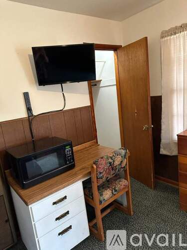 A small room with a microwave, a TV, a chair and a bed.