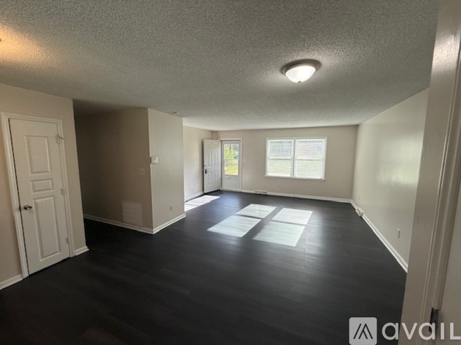 A room with a white door and a window with a view of a lawn and trees.