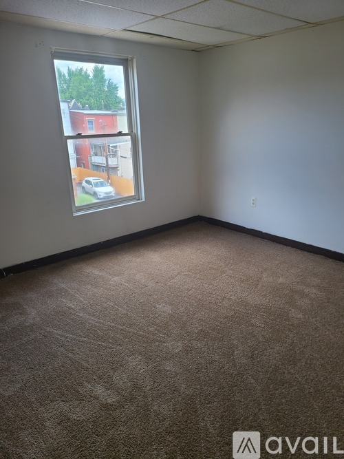 A room with a carpeted floor and a window showing a view of a red building.