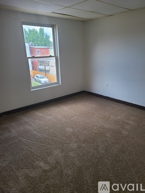 A room with a carpeted floor and a window showing a view of a red building.