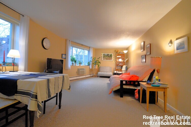 A bedroom with a bed, a couch, a chair, a table, and a television.