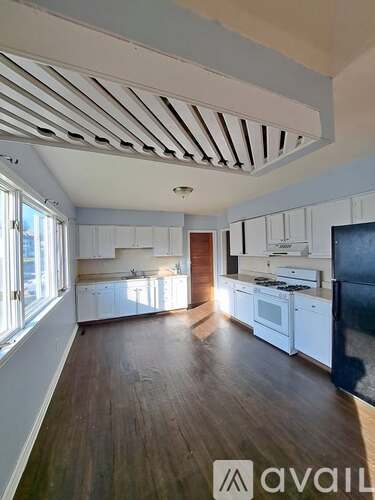 A spacious kitchen with white cabinets and a black refrigerator.
