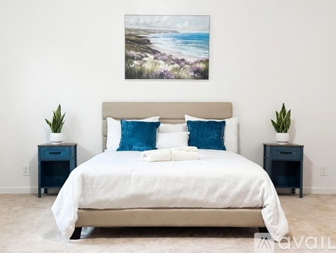 A bedroom with a large bed and a painting of a beach scene on the wall.