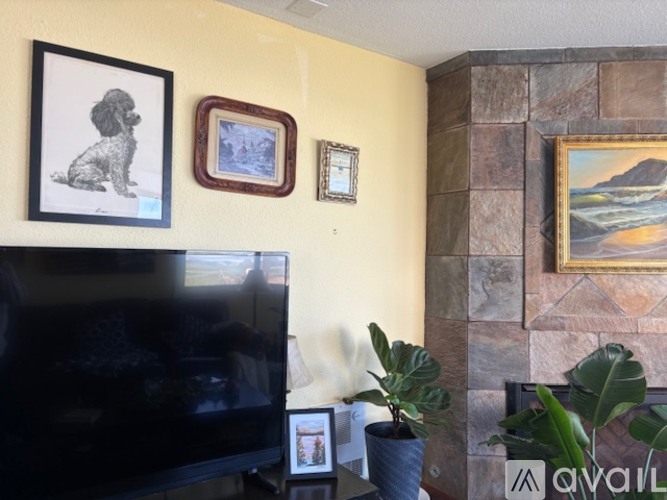 A living room with a flat screen TV, a dog picture, a landscape picture, a plant and a fireplace.