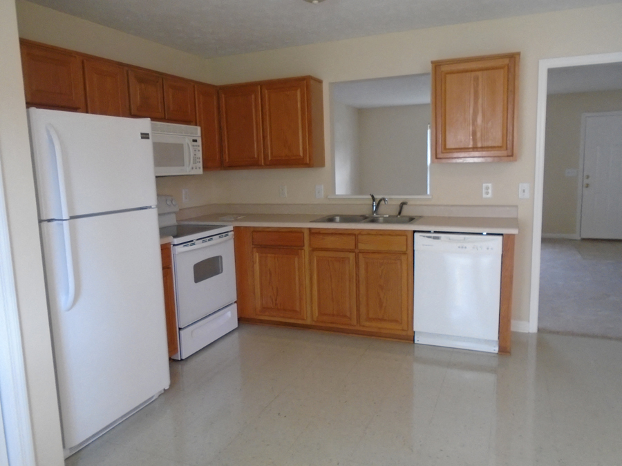 an empty kitchen with white appliances and wooden cabinets