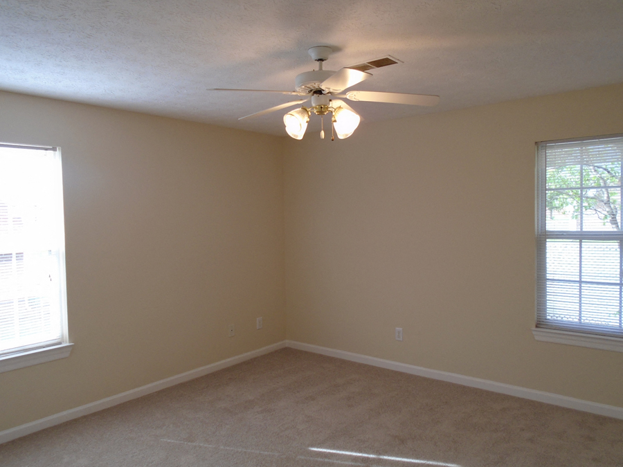 a bedroom with a ceiling fan and two windows