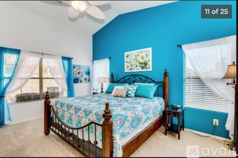 A bedroom with a bed, a ceiling fan, and a window with blue curtains.