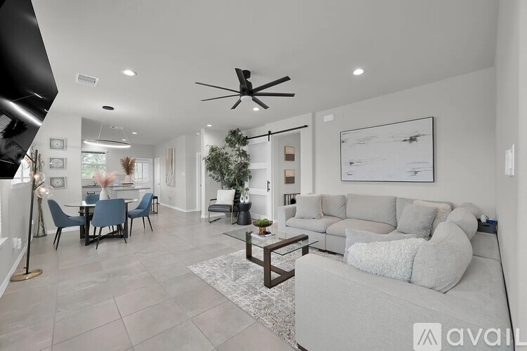 A spacious living room with a grey sofa and a dining table with chairs.