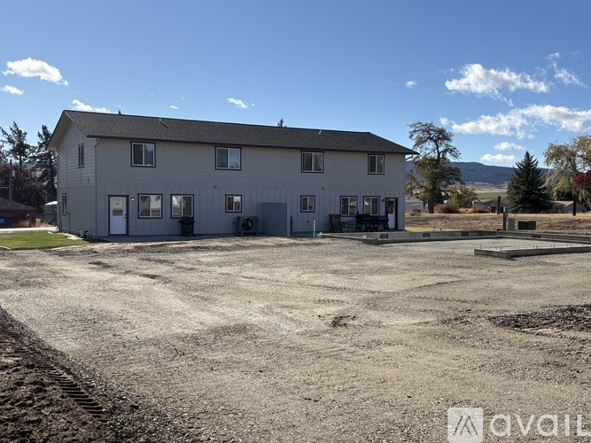 A house with a grey exterior is surrounded by a gravel lot.