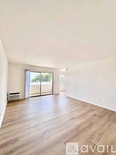 A spacious room with wooden flooring and a sliding glass door leading to a balcony.