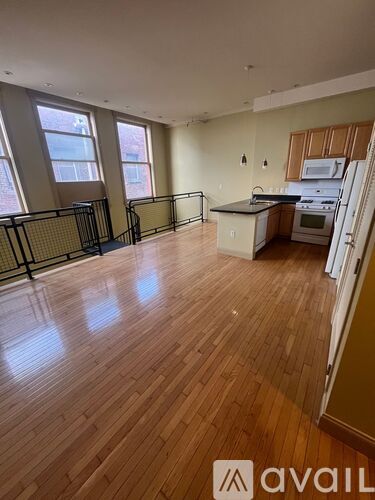A large empty room with wooden floors and a kitchen area in the background.