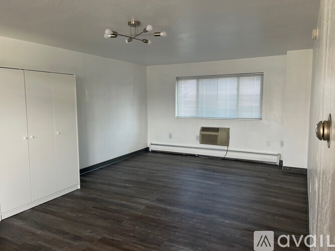 A room with wooden floors and white walls, with a window and a door visible.
