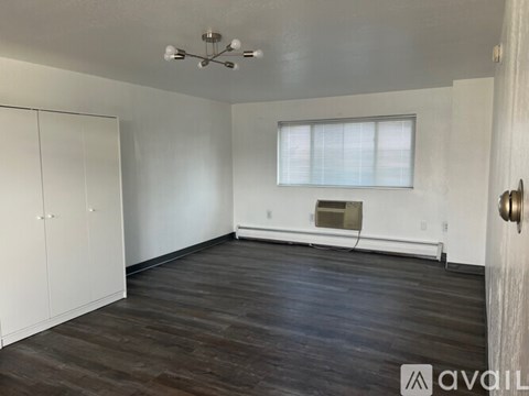A room with wooden floors and white walls, with a window and a door visible.