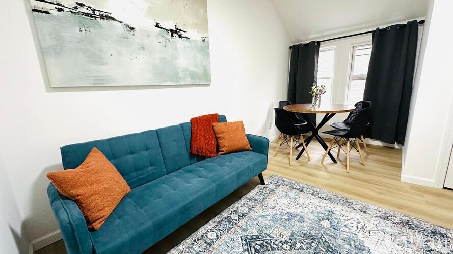 A blue couch with orange pillows sits in a room with a painting on the wall.