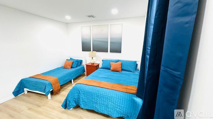 Three beds with blue bedspreads and orange pillows in a room.