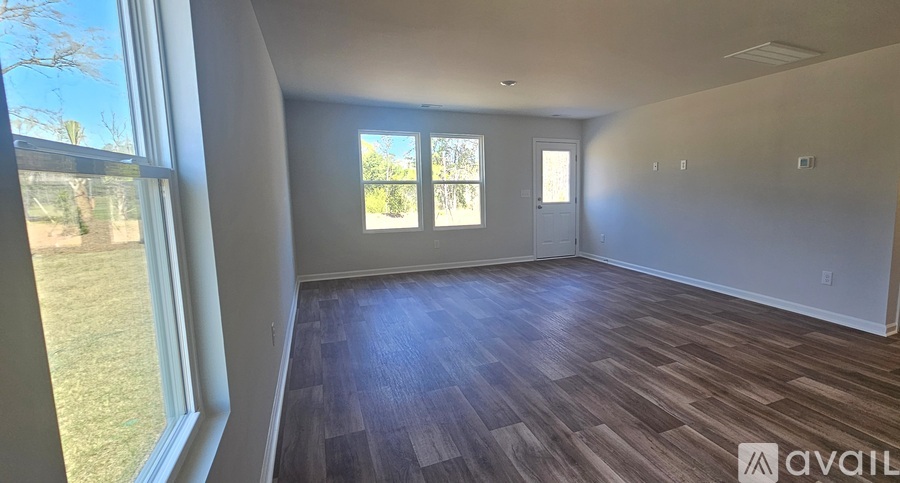 A room with wooden flooring and a large window overlooking a grassy area.