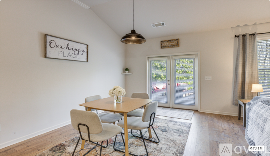 A dining room with a wooden table and chairs, a sign on the wall saying "Our happy place", and a view of the backyard through the sliding glass doors.