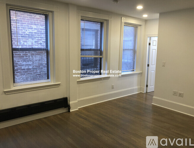 A room with wooden floors and three windows.