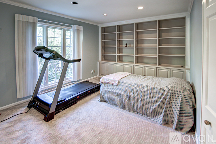 A treadmill is in the corner of a bedroom with a bed and shelves.