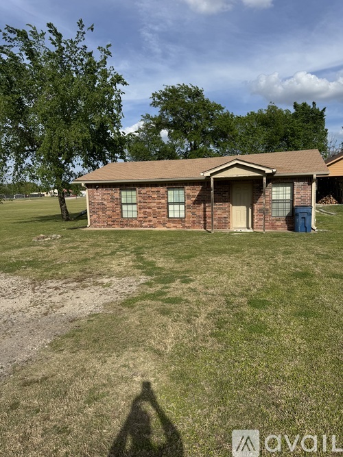 A house with a brown roof and a blue trash can in front of it.