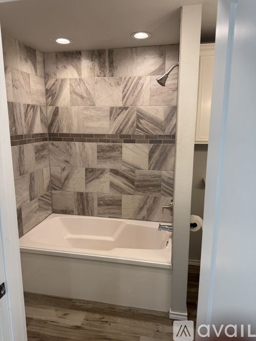 A bathroom with a marble tile wall and a white bathtub.