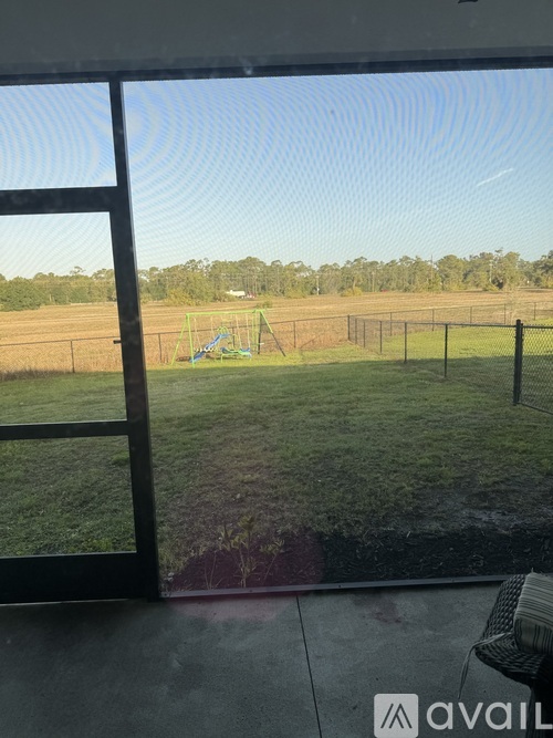 A view from a window looking out to a playground and a fence.