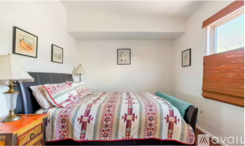 A bedroom with a bed, a nightstand with a lamp, and pictures on the wall.