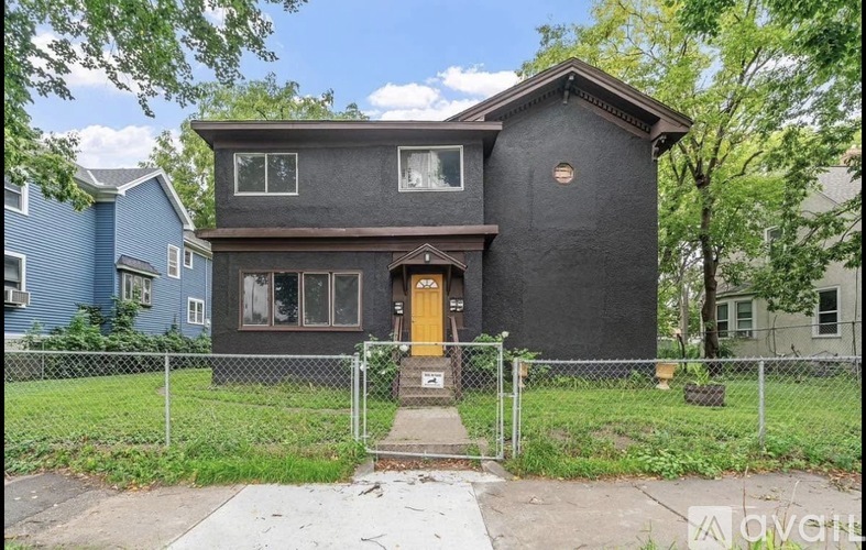 A black house with a yellow door is surrounded by a fence.