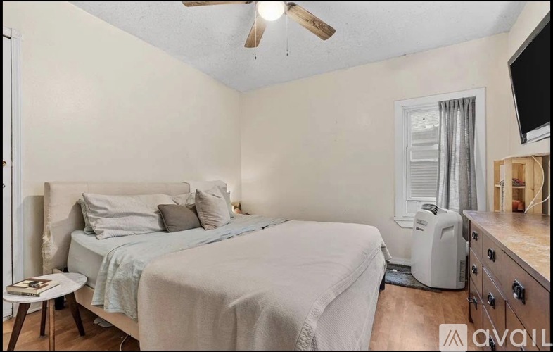 A bedroom with a bed, a ceiling fan, and a window with a white air conditioner.