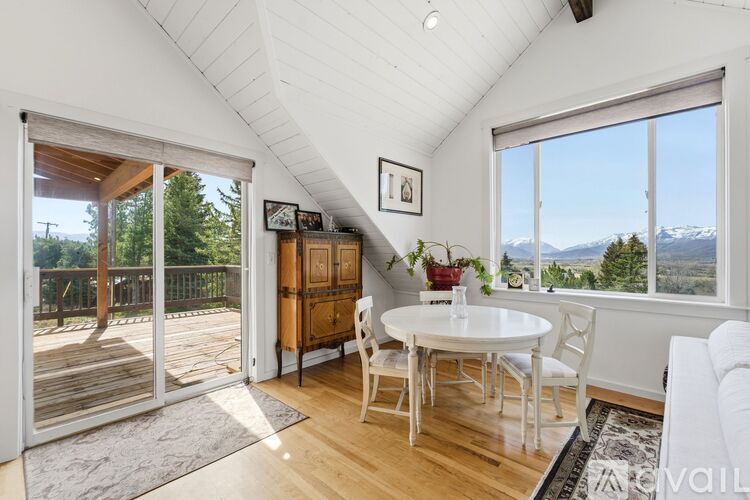 A white dining room with a table and chairs and a view of the mountains.