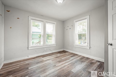 A room with wooden flooring and two windows.