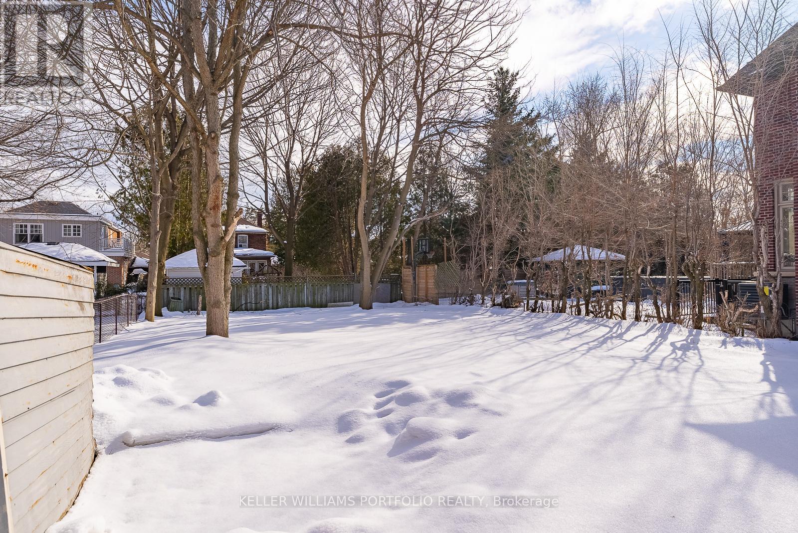 A snow-covered yard with a fence and bare trees.