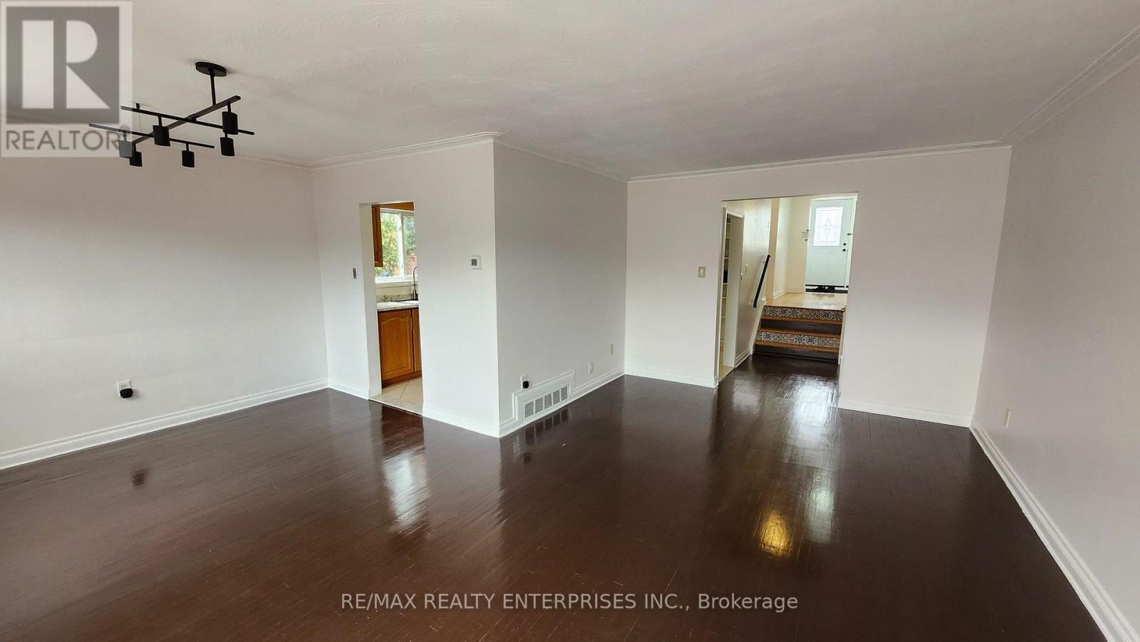 A spacious room with wooden floors and white walls, with a chandelier hanging from the ceiling.