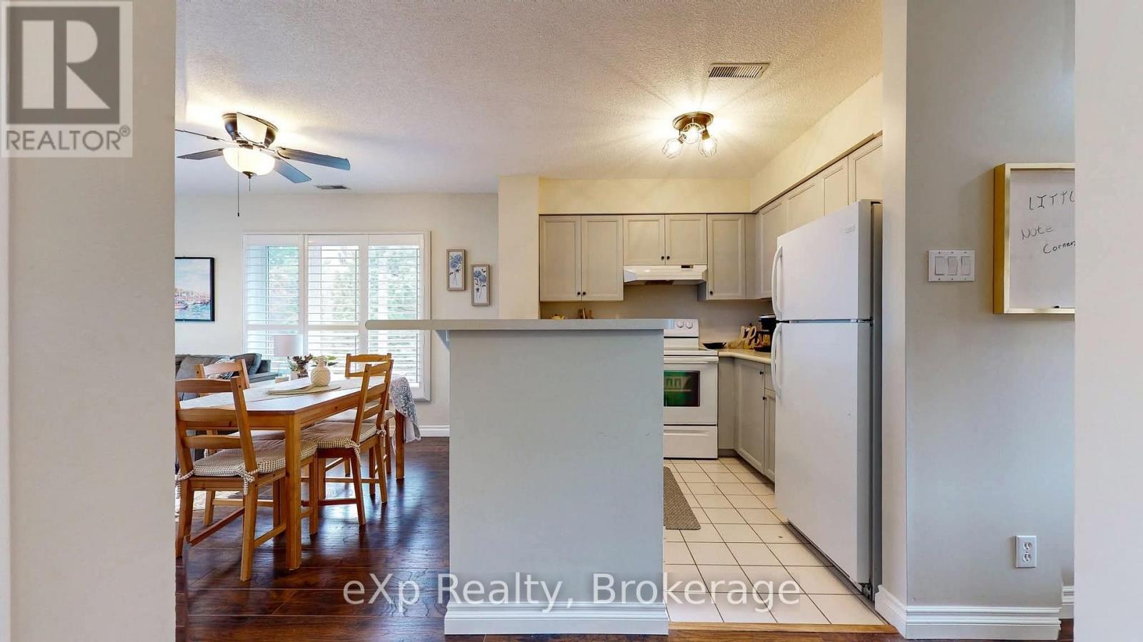 A kitchen with white appliances and wooden chairs.