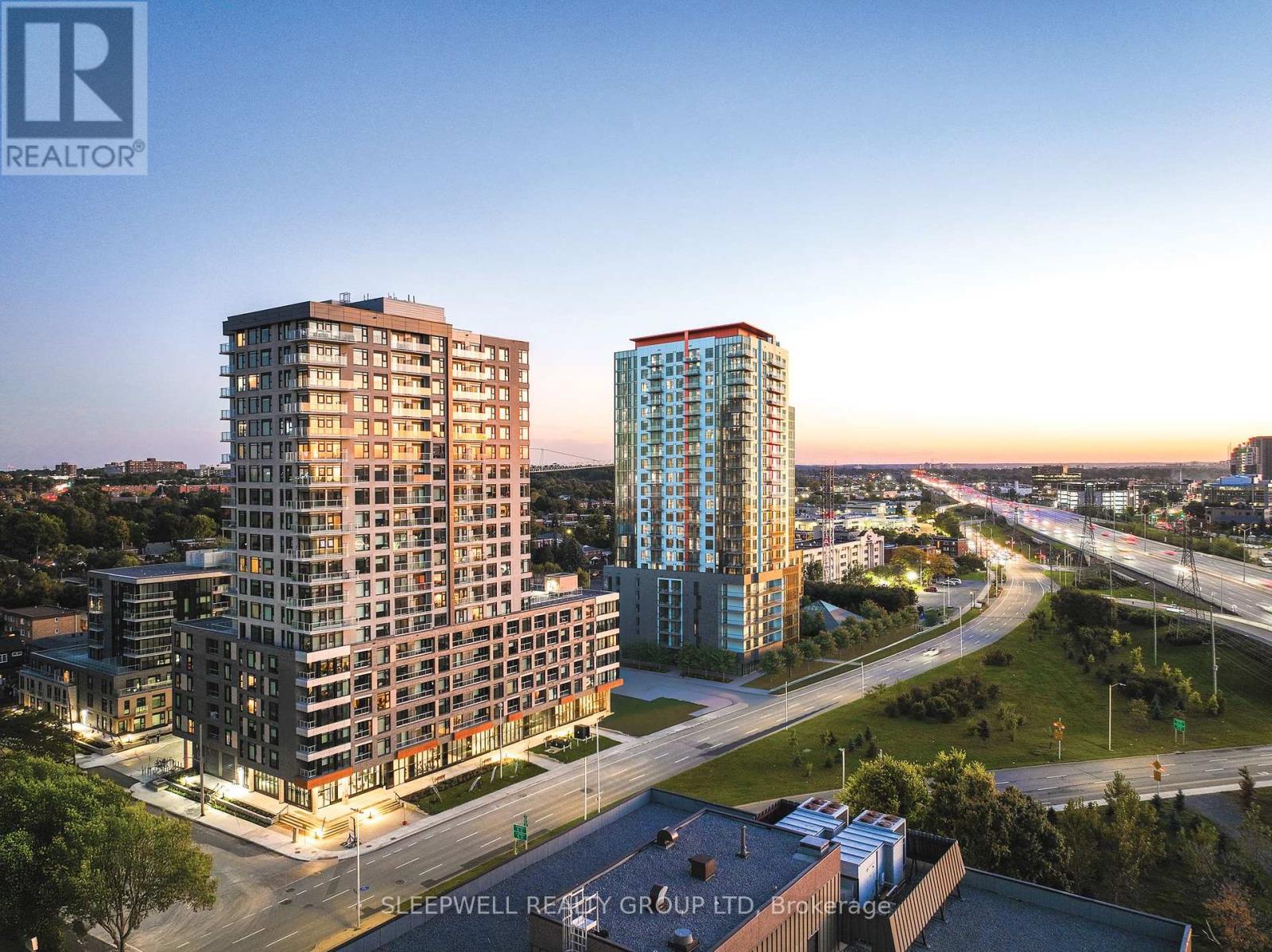 Two high-rise buildings are shown in an aerial view with a roadway in front of them.