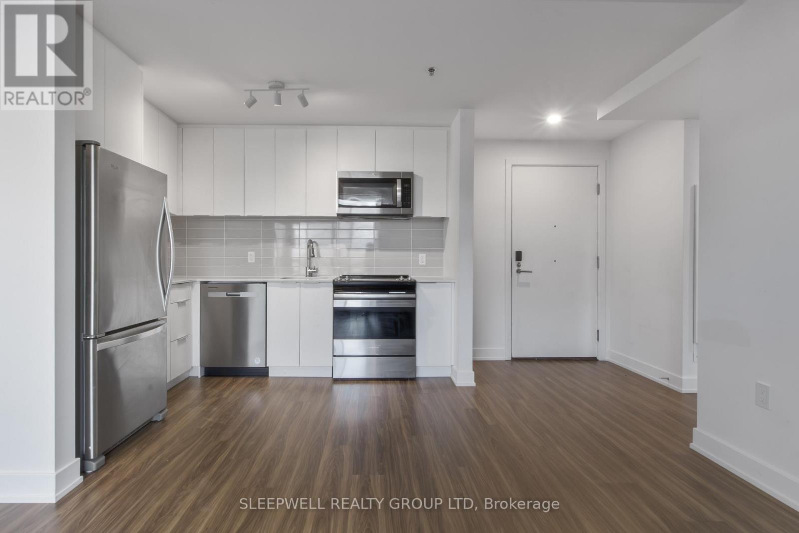 A modern kitchen with stainless steel appliances and wooden flooring.