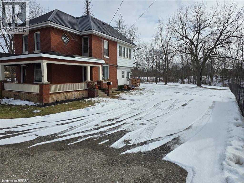 A red brick house with a white porch and a snow covered driveway.