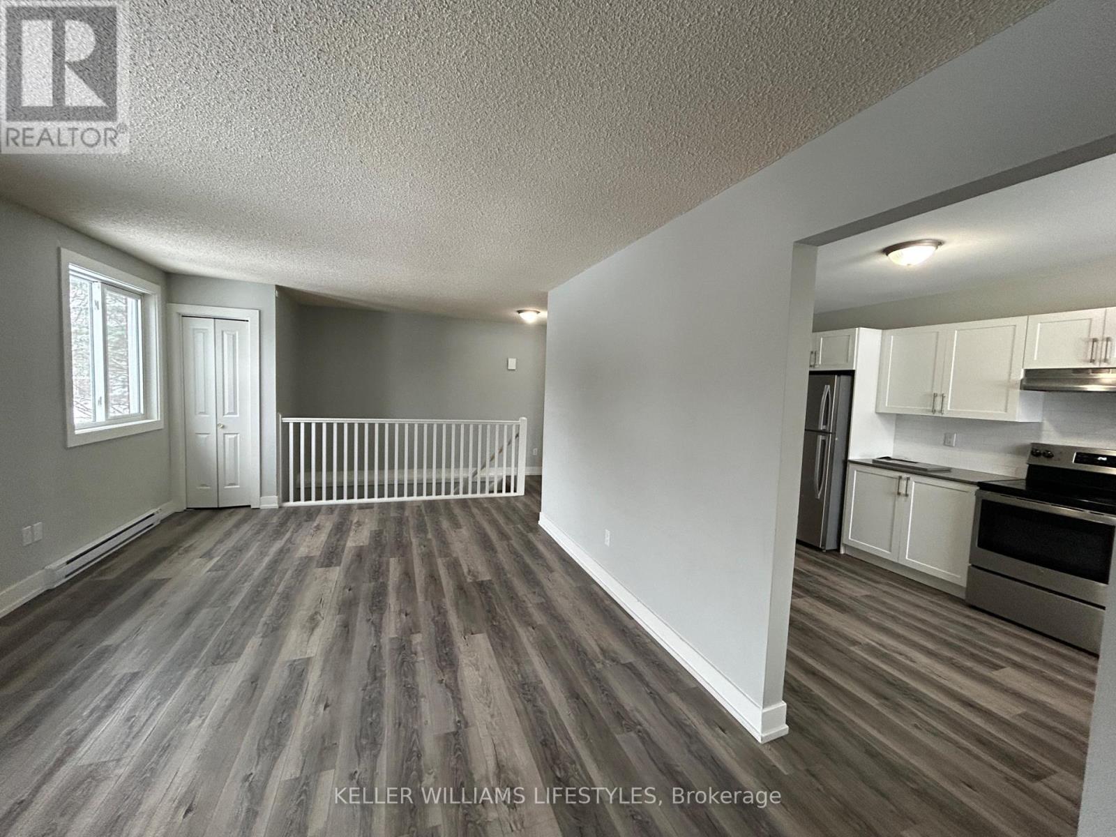 A spacious living room with wood flooring and a kitchen area in the background.