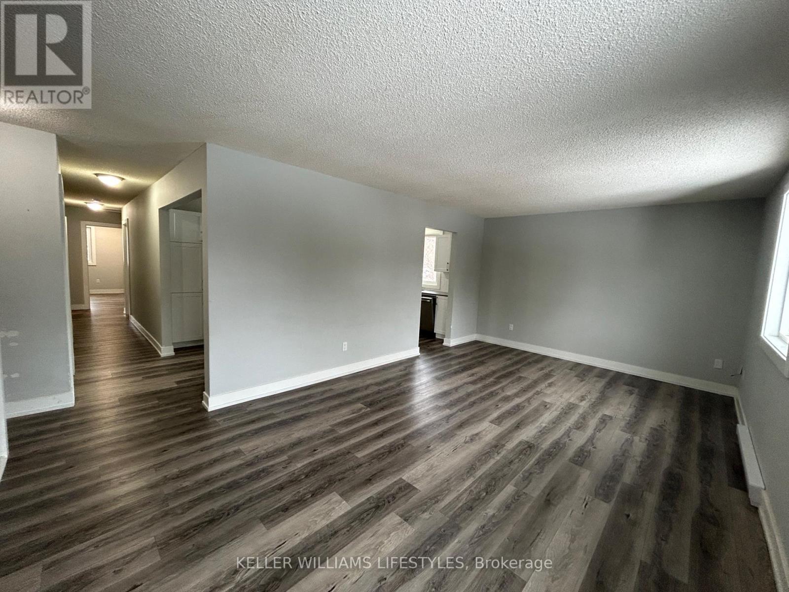 A spacious room with wood flooring and white walls.