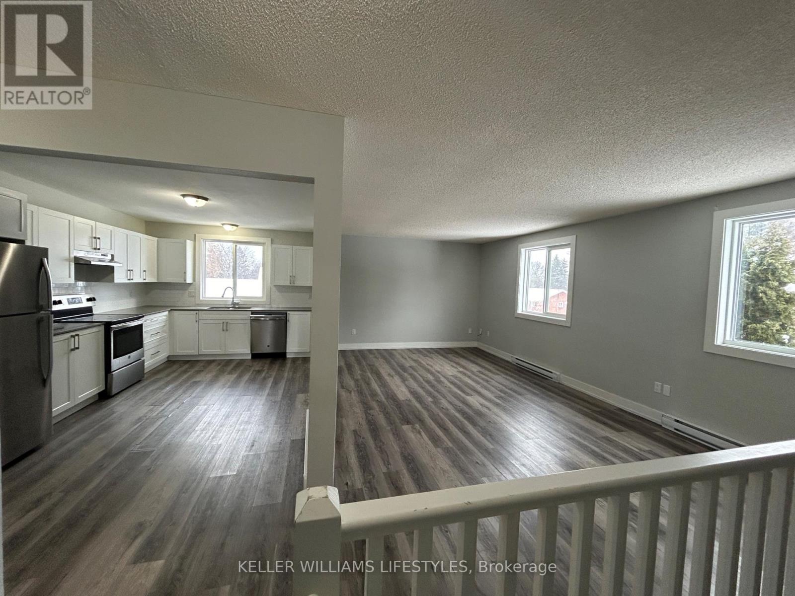 A spacious kitchen and living room with wood flooring and white walls.