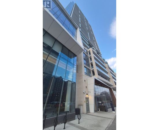 A modern building with a glass facade and a tall tower in the background.